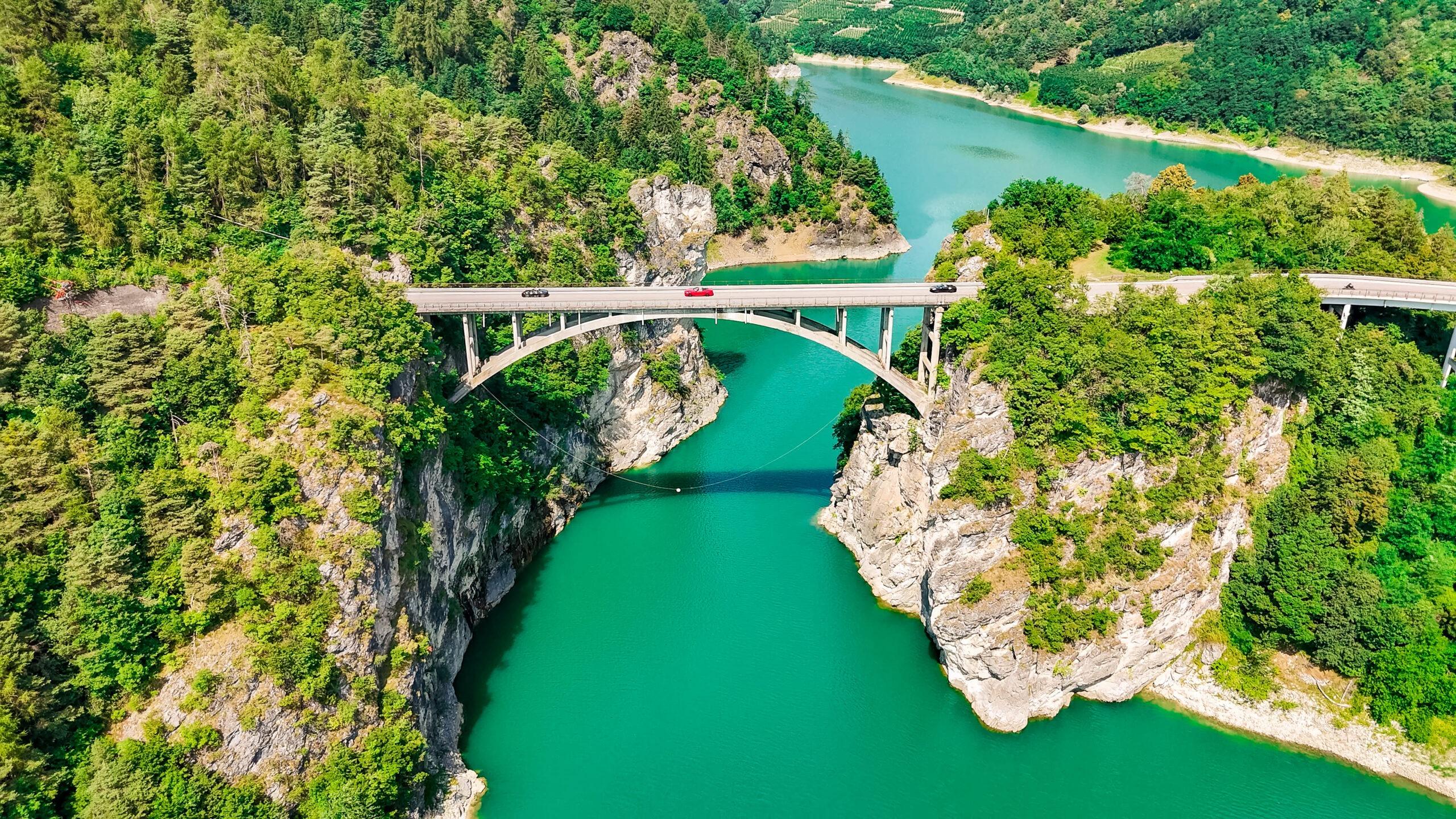 Luftaufnahme einer Brücke über einen türkisen See, befahren auf der Tour di Trentino Sportwagen Erlebnisreise.