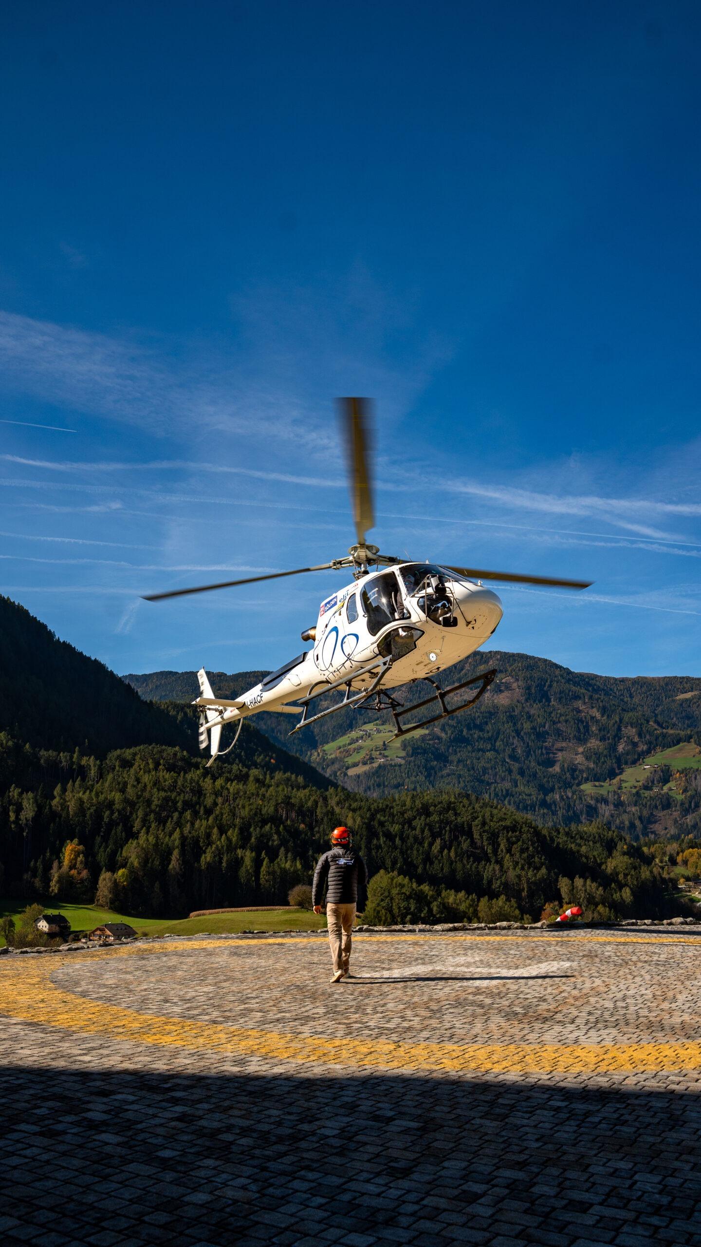Hubschrauber landet in malerischer Berglandschaft der Alpen unter klarem, blauem Himmel.