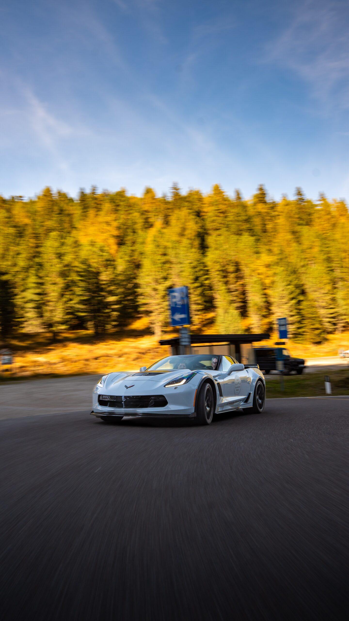 Weiße Corvette Cabrio fährt dynamisch durch eine Kurve vor herbstlichem Wald bei der Sportwagen Erlebnisreise.